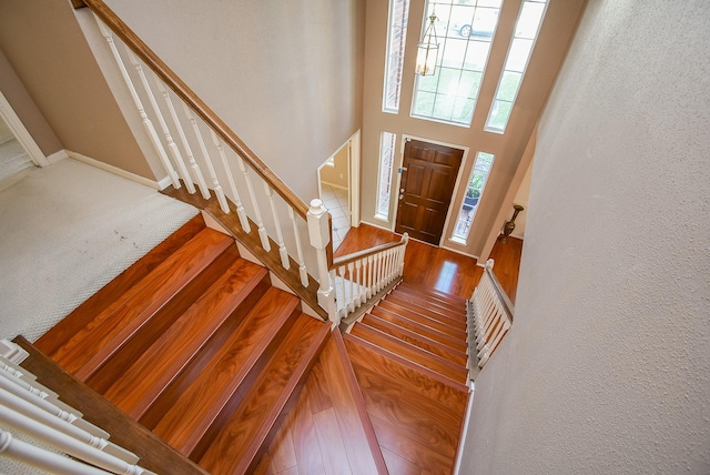 entryway with stairway, baseboards, a towering ceiling, wood-type flooring, and a textured wall