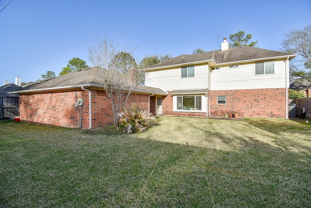 back of house featuring fence, brick siding, a chimney, and a lawn