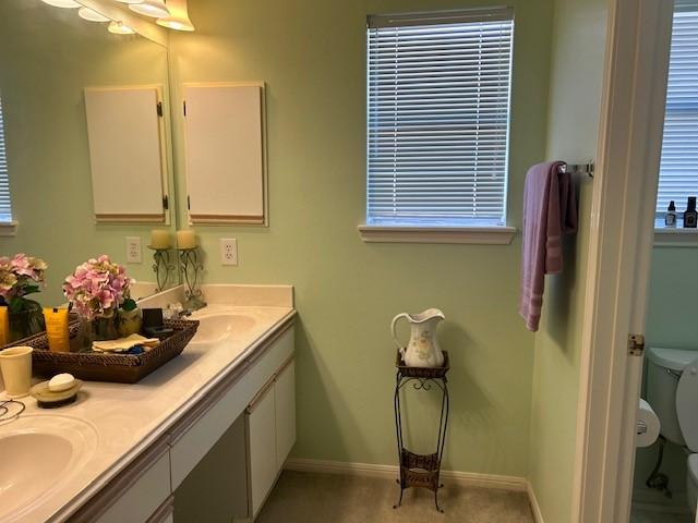 full bath featuring double vanity, a sink, toilet, and baseboards