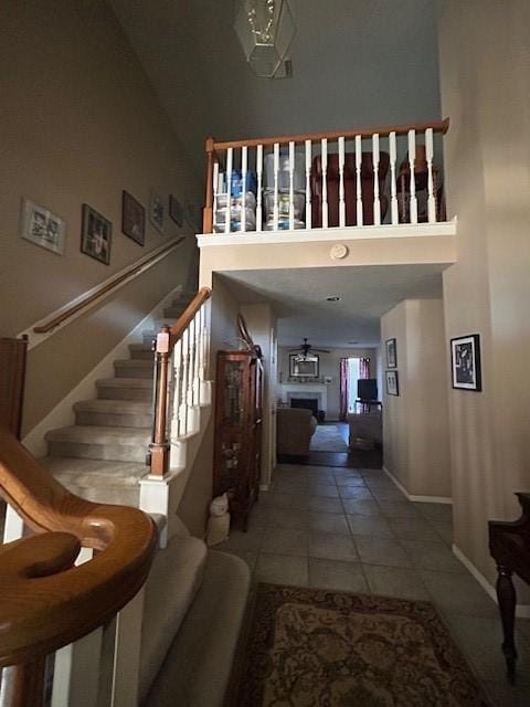 stairway with a fireplace, a towering ceiling, baseboards, and tile patterned floors