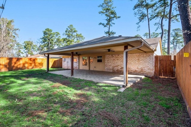 back of house with stone siding, a fenced backyard, a yard, and a patio