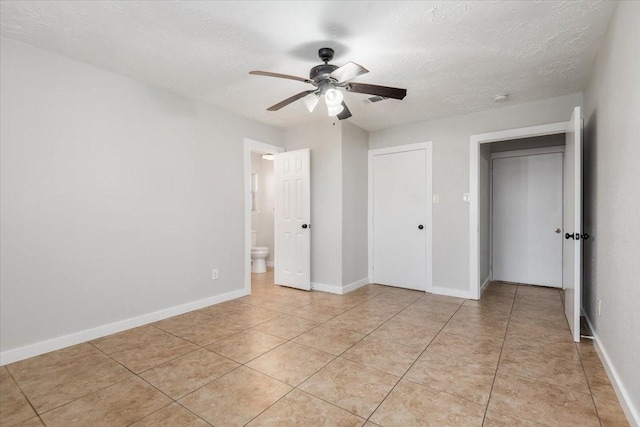 unfurnished bedroom with light tile patterned floors, baseboards, a ceiling fan, ensuite bath, and a textured ceiling