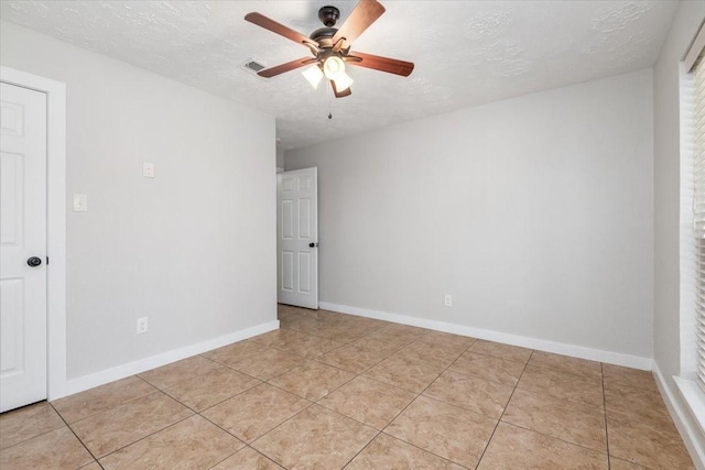 empty room with a textured ceiling, light tile patterned flooring, visible vents, baseboards, and a ceiling fan