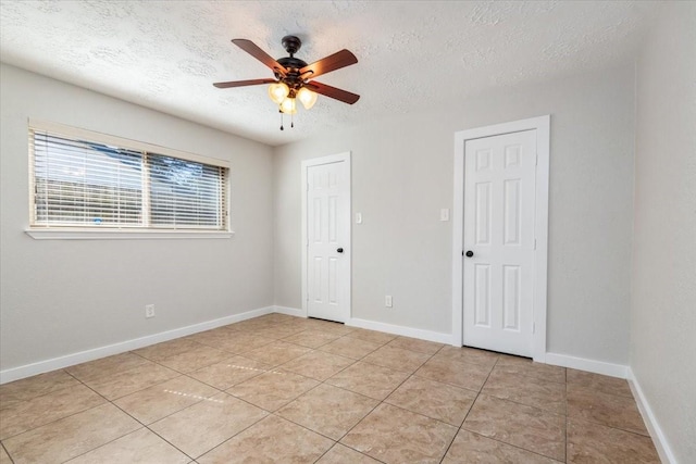 empty room with light tile patterned floors, a textured ceiling, a ceiling fan, and baseboards