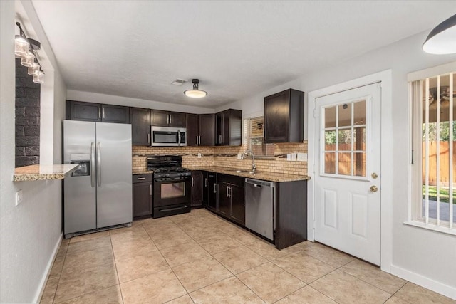 kitchen with stainless steel appliances, backsplash, a sink, and light stone countertops