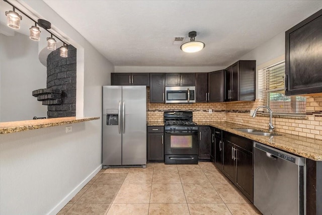 kitchen with light tile patterned floors, light stone countertops, stainless steel appliances, a sink, and decorative backsplash