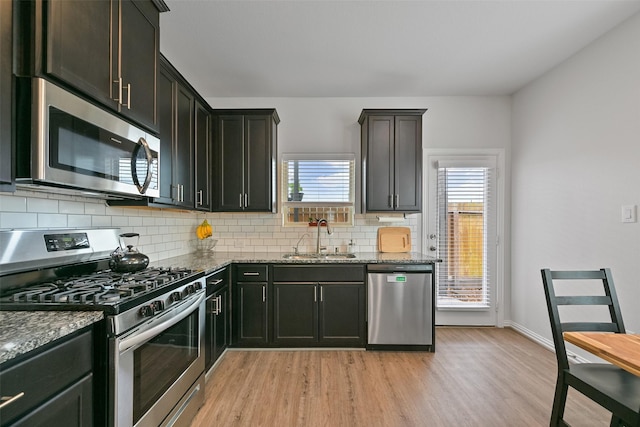 kitchen with stone countertops, decorative backsplash, light wood-style flooring, stainless steel appliances, and a sink