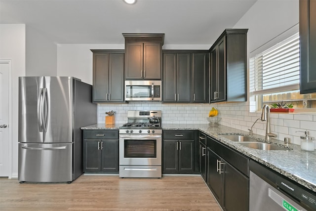 kitchen with decorative backsplash, light stone countertops, stainless steel appliances, light wood-style floors, and a sink