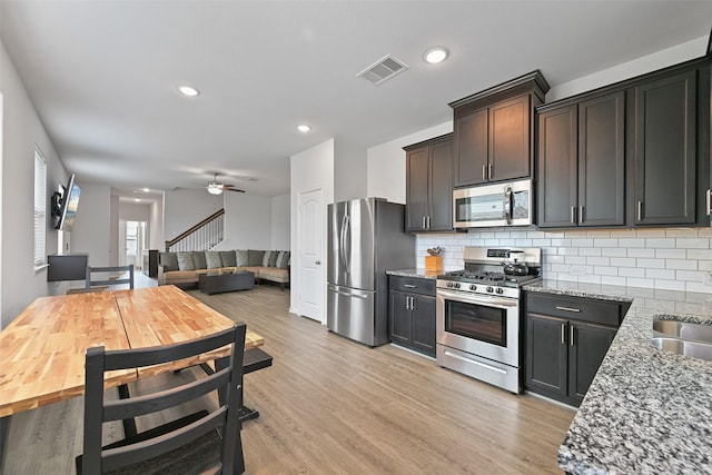 kitchen featuring light wood finished floors, visible vents, light stone countertops, stainless steel appliances, and backsplash