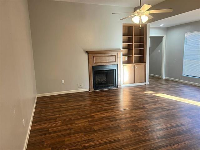 unfurnished living room featuring ceiling fan, dark wood-type flooring, a fireplace, and baseboards