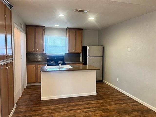 kitchen featuring dark wood-style floors, freestanding refrigerator, visible vents, and a center island with sink