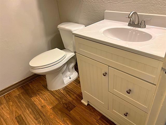 half bathroom with a textured wall, toilet, wood finished floors, vanity, and baseboards