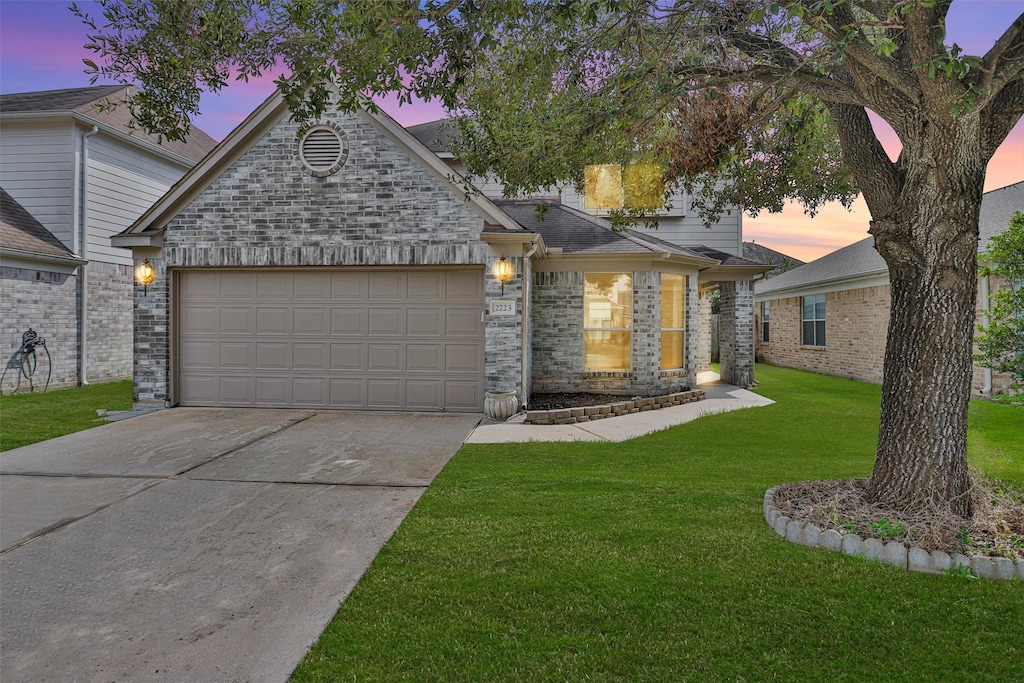 view of front facade featuring brick siding, a lawn, driveway, and an attached garage