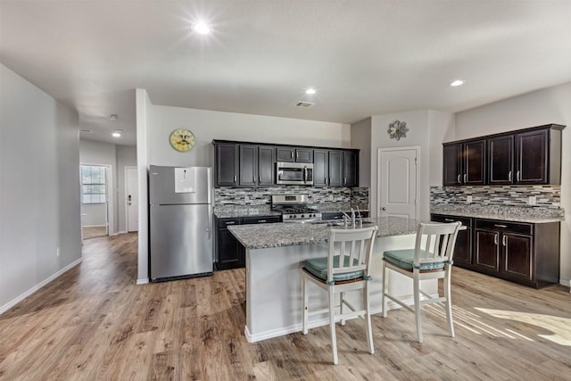 kitchen featuring tasteful backsplash, visible vents, light wood-style flooring, appliances with stainless steel finishes, and an island with sink