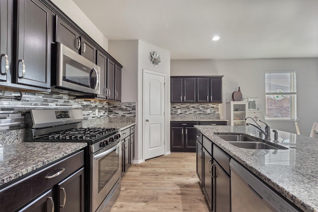 kitchen with appliances with stainless steel finishes, light wood-type flooring, a sink, and light stone counters