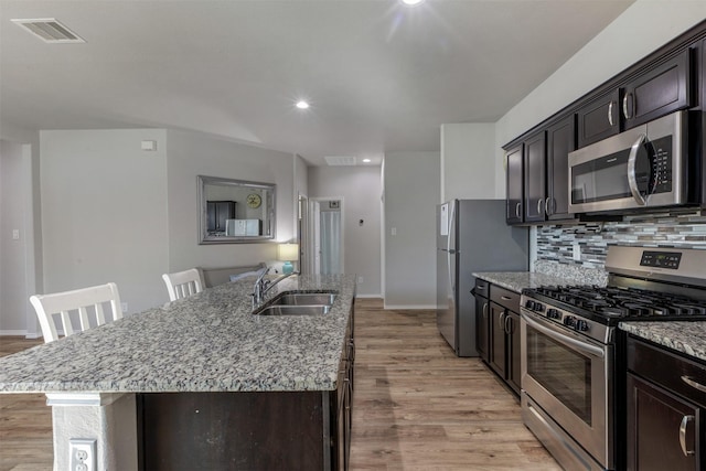 kitchen featuring a center island with sink, visible vents, light stone countertops, stainless steel appliances, and a sink