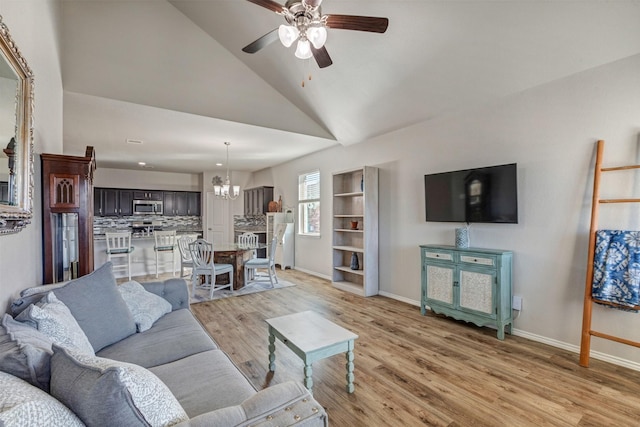 living area with ceiling fan with notable chandelier, high vaulted ceiling, light wood-type flooring, and baseboards