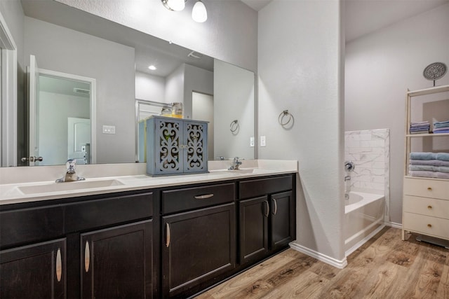 full bath featuring double vanity, a garden tub, a sink, and wood finished floors