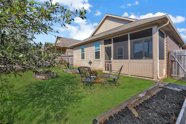 rear view of property with a vegetable garden, a lawn, a sunroom, fence, and brick siding