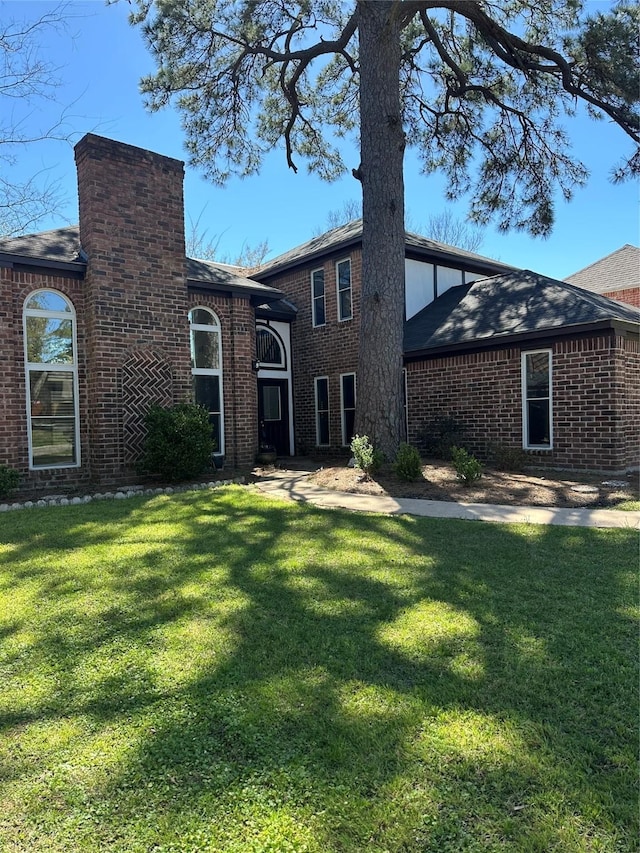 back of house featuring brick siding, a yard, and a chimney