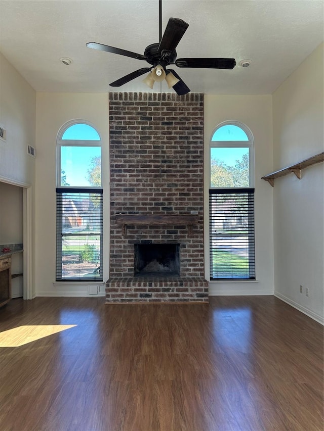 unfurnished living room featuring a wealth of natural light, ceiling fan, a fireplace, and wood finished floors