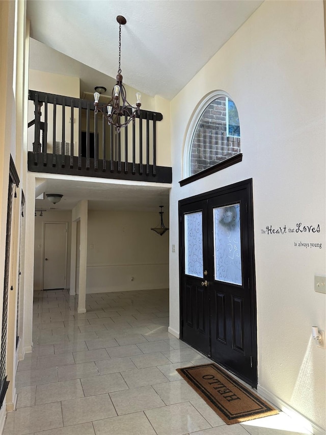 foyer entrance with baseboards, high vaulted ceiling, a chandelier, and french doors