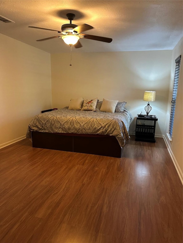 bedroom featuring dark wood finished floors, visible vents, a ceiling fan, a textured ceiling, and baseboards