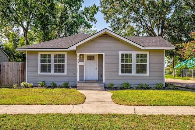 bungalow-style home with a front lawn, roof with shingles, and fence