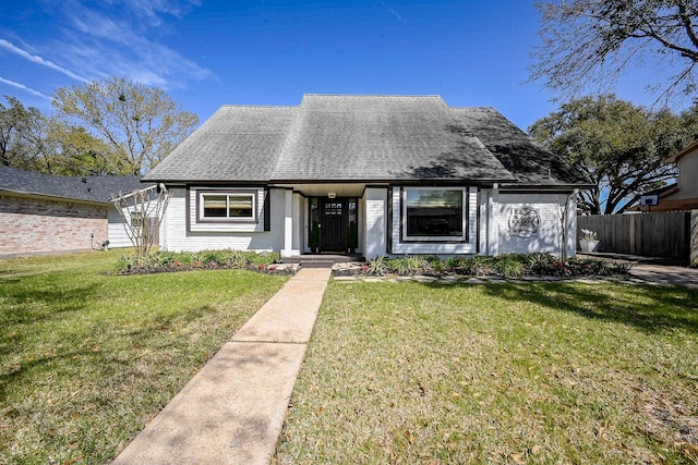 view of front of home with brick siding, a shingled roof, a front yard, and fence