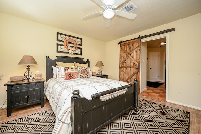 bedroom with a barn door, baseboards, visible vents, and light wood-style flooring