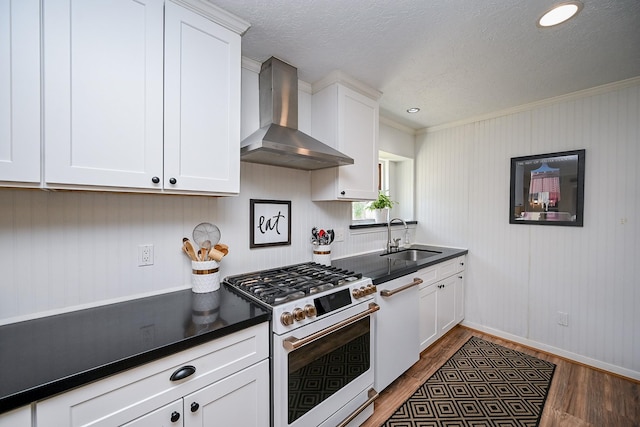 kitchen with white appliances, wood finished floors, a sink, white cabinetry, and wall chimney range hood