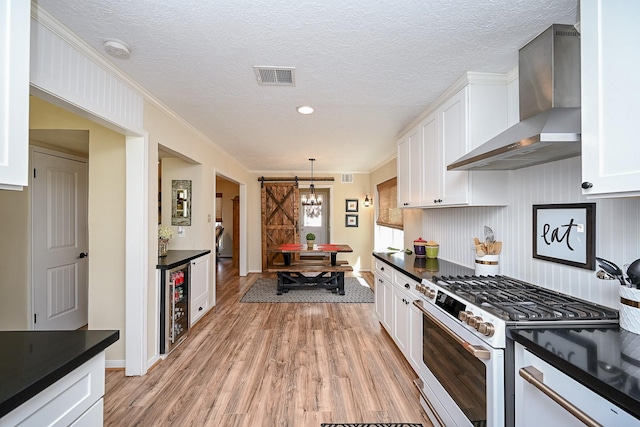 kitchen featuring dark countertops, white range with gas cooktop, wall chimney exhaust hood, and visible vents