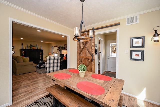 dining room featuring a barn door, a textured ceiling, visible vents, and wood finished floors