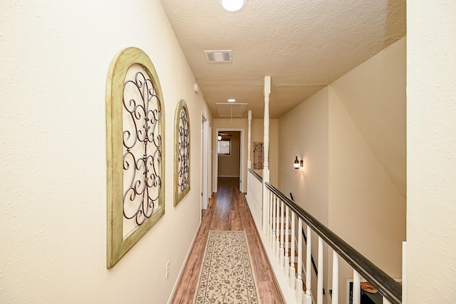 hall with attic access, wood finished floors, visible vents, and a textured ceiling