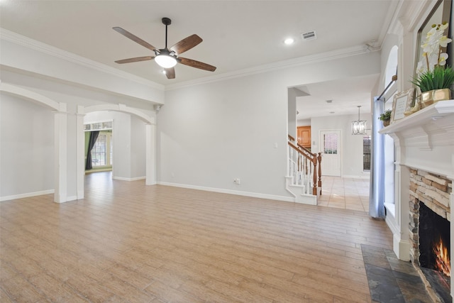 unfurnished living room featuring arched walkways, visible vents, light wood-style flooring, ornamental molding, and a stone fireplace