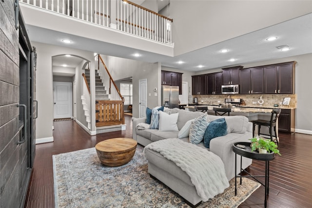 living area featuring dark wood-style floors, arched walkways, a high ceiling, baseboards, and stairs