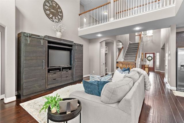 living room with dark wood-style floors, stairs, a towering ceiling, and baseboards