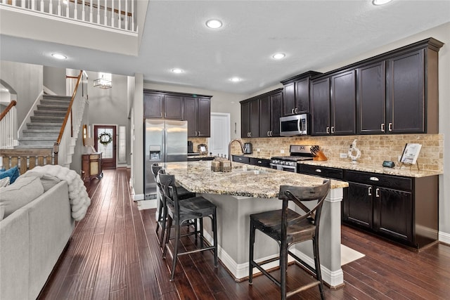 kitchen with a breakfast bar, dark wood-type flooring, open floor plan, light stone countertops, and stainless steel appliances