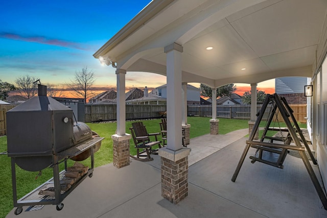 patio terrace at dusk featuring a fenced backyard and a lawn