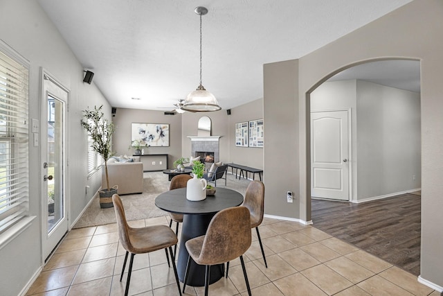 dining area with a warm lit fireplace, baseboards, arched walkways, and light tile patterned flooring