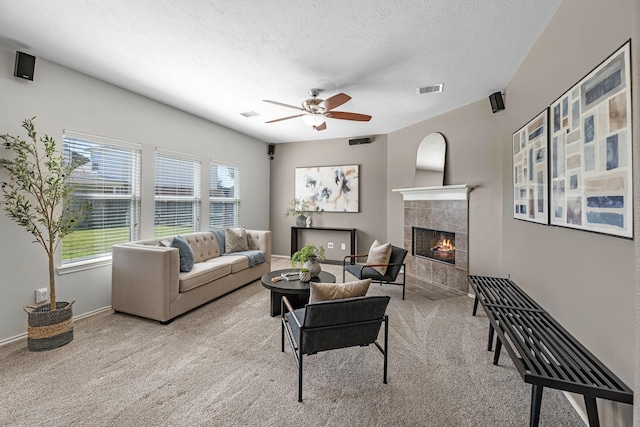 living room with visible vents, a ceiling fan, light colored carpet, a textured ceiling, and a fireplace