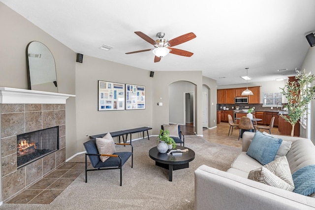 living room featuring visible vents, arched walkways, a tiled fireplace, ceiling fan, and light tile patterned flooring