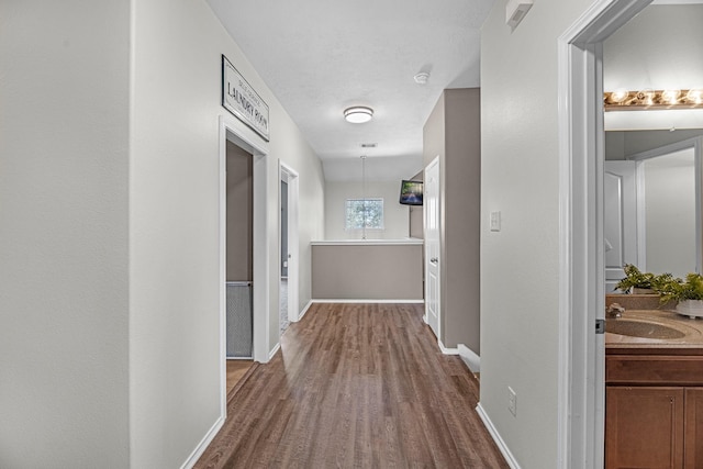 corridor featuring dark wood-style flooring, a sink, and baseboards