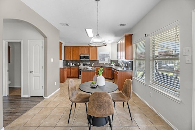 dining space with light tile patterned floors, arched walkways, visible vents, and baseboards