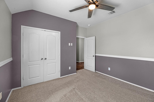 unfurnished bedroom with carpet floors, lofted ceiling, a closet, visible vents, and a ceiling fan