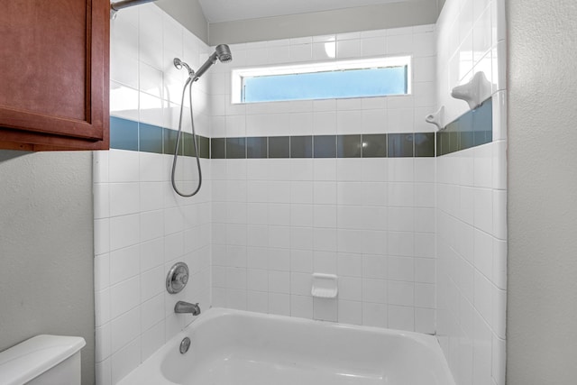 full bath with toilet, washtub / shower combination, and a textured wall