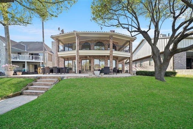 rear view of property with brick siding, a patio, a yard, and a balcony