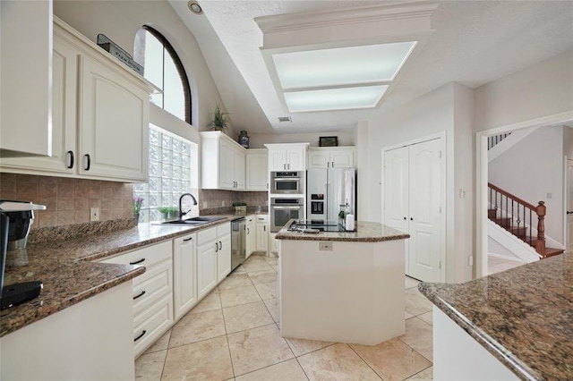 kitchen with dark stone counters, stainless steel appliances, a kitchen island, and a sink