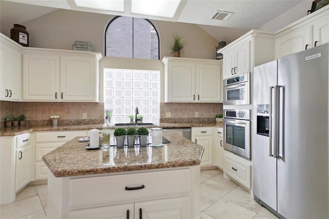 kitchen with light stone counters, a center island, visible vents, appliances with stainless steel finishes, and vaulted ceiling