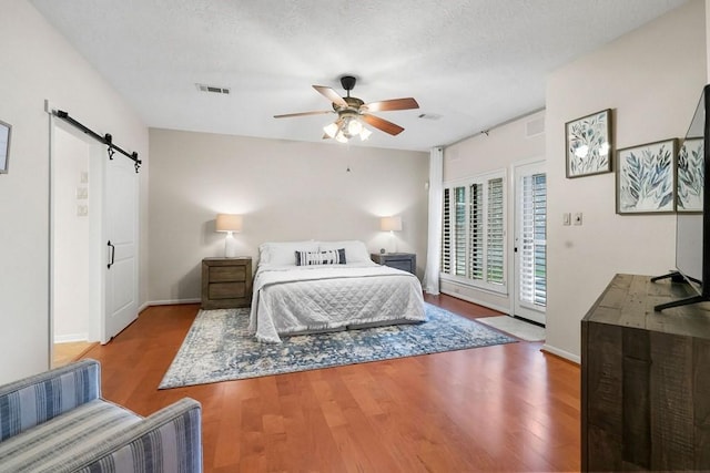 bedroom with a textured ceiling, a barn door, wood finished floors, visible vents, and access to exterior